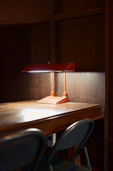 Warmly lit vintage desk with classic banker's lamp and two chairs in a study room.