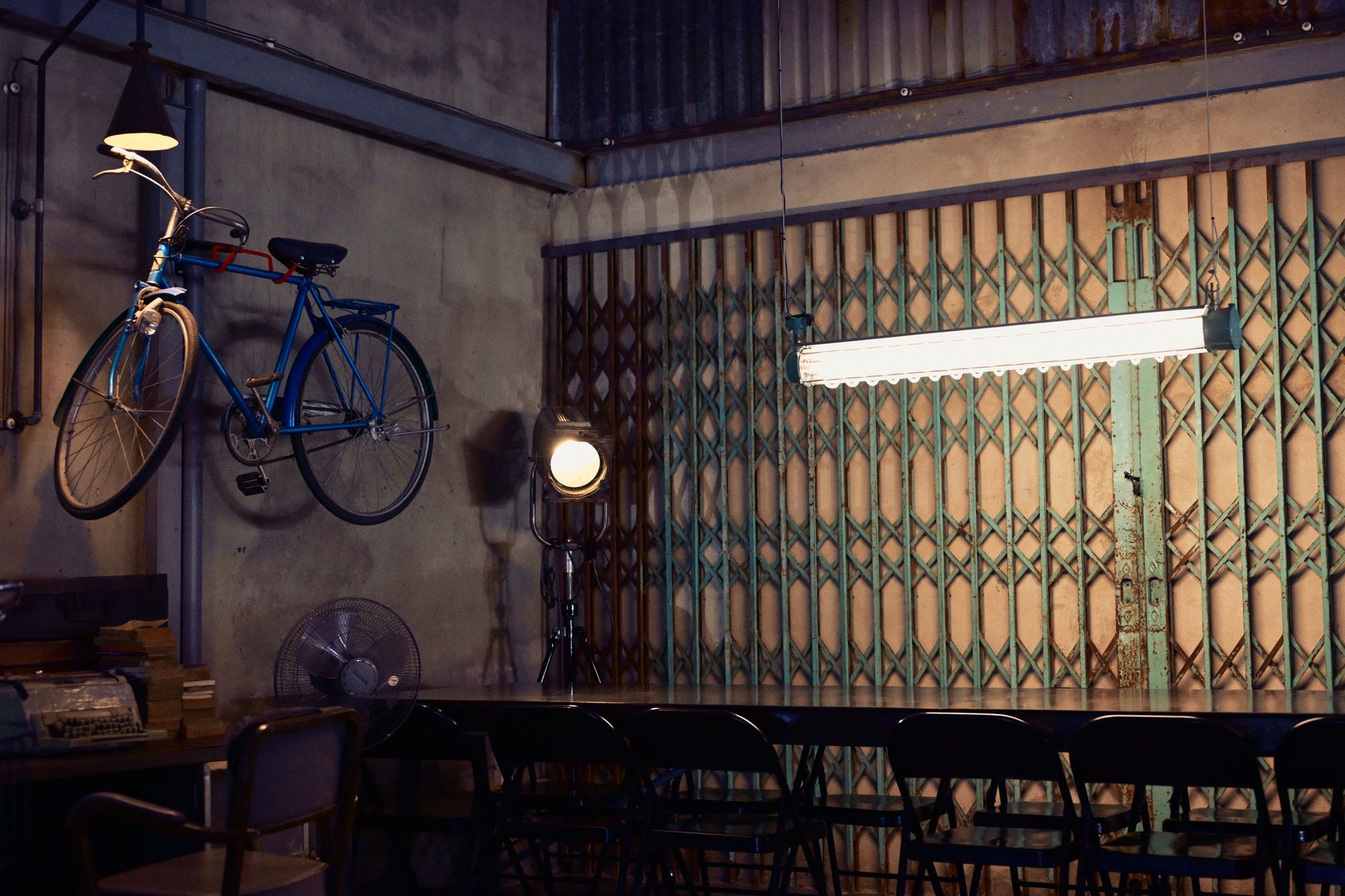 A vintage industrial loft interior featuring a bicycle wall decor, retro lighting, and folding chairs, creating an eclectic ambiance.