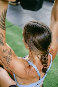 Fit woman with tattoo and braided hair exercising indoors on a green mat.