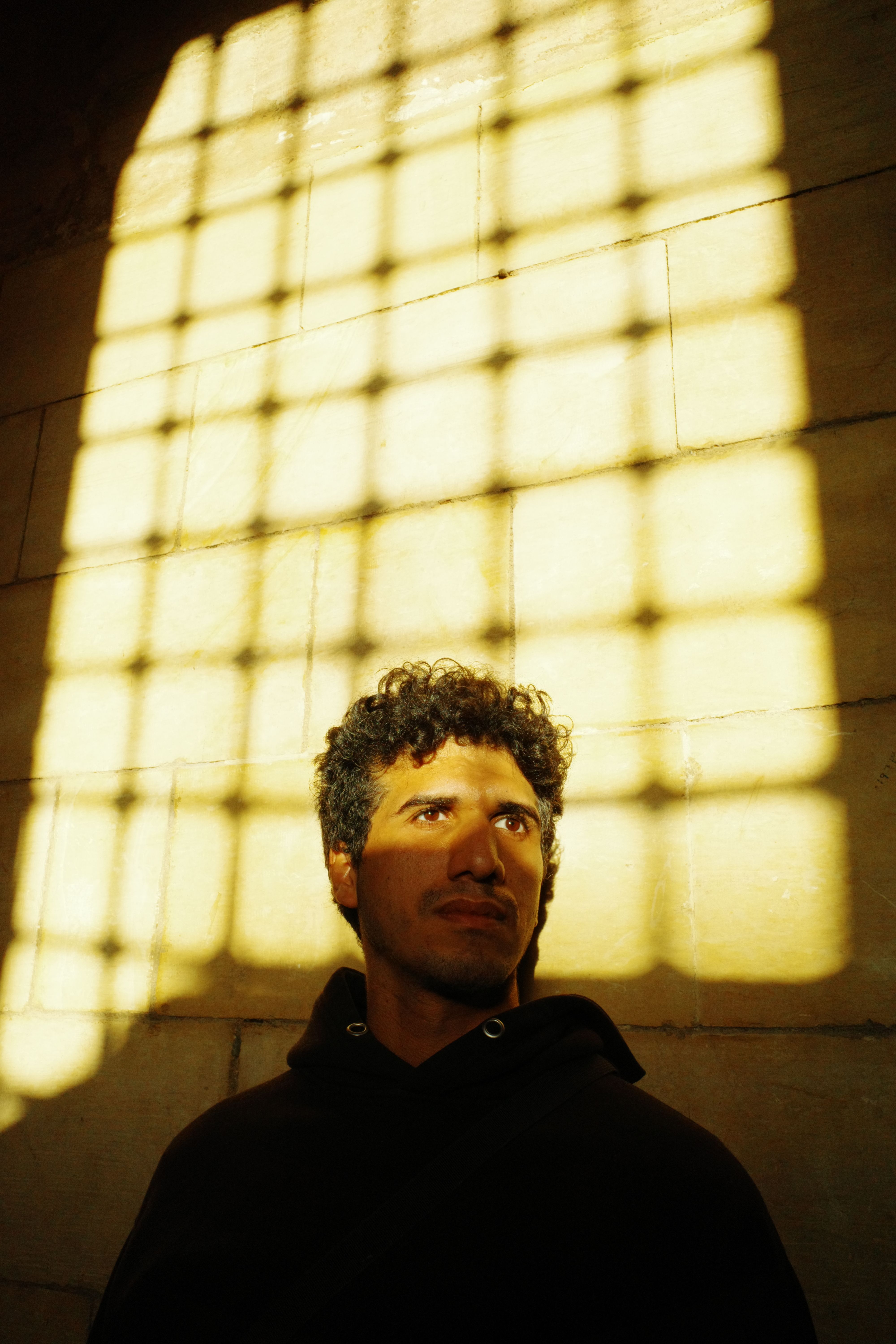 A dramatic portrait of a person in a sunlit interior grid pattern.