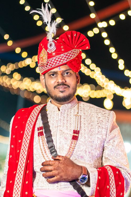 Free Indian groom wearing a traditional red turban and sherwani during an evening wedding ceremony with festive lights. Stock Photo
