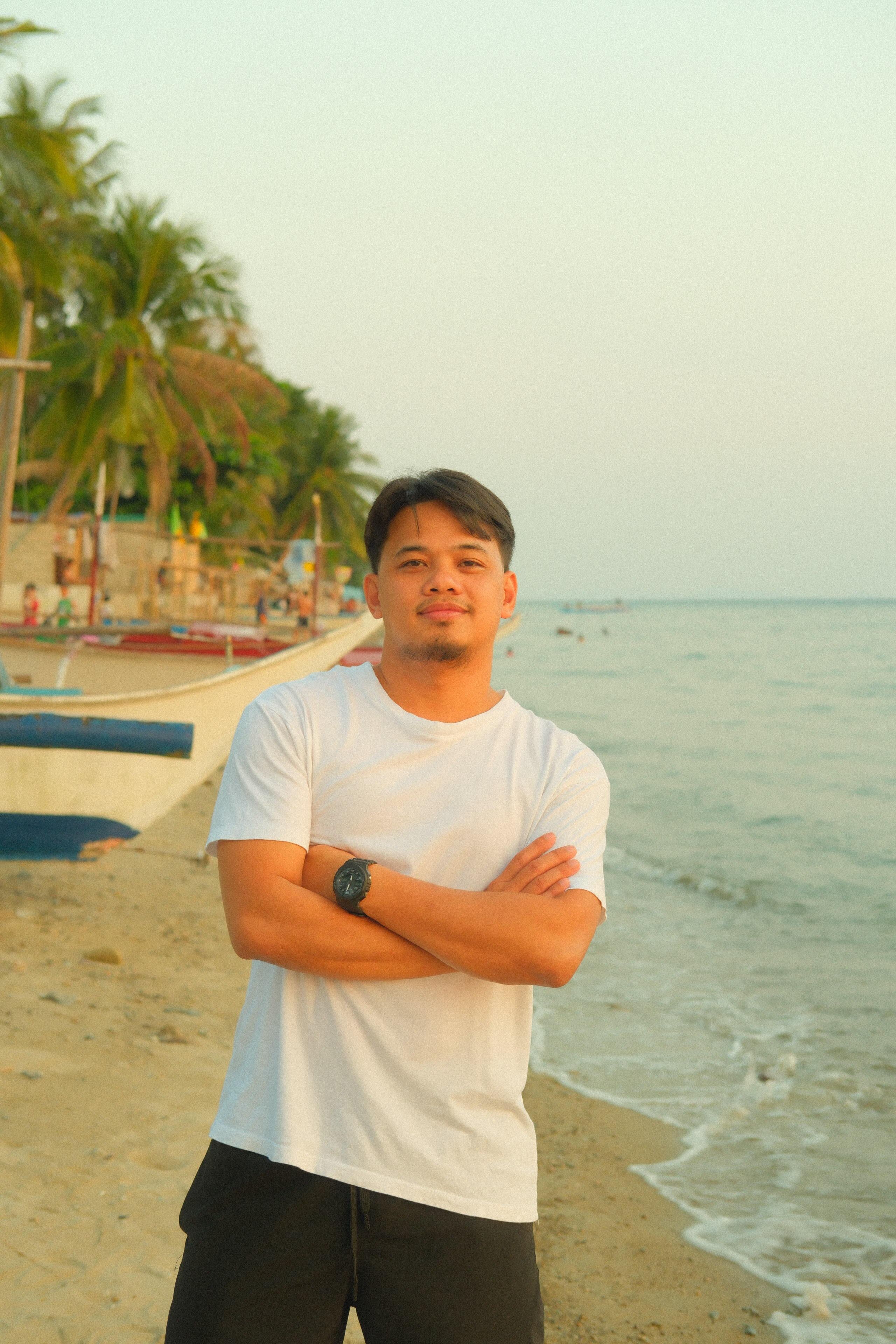 A man stands confidently on a palm-lined beach, enjoying a sunset by the ocean.