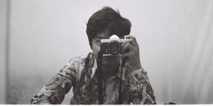 A black and white self-portrait featuring a person holding a vintage camera, reflecting a classic and artistic style.