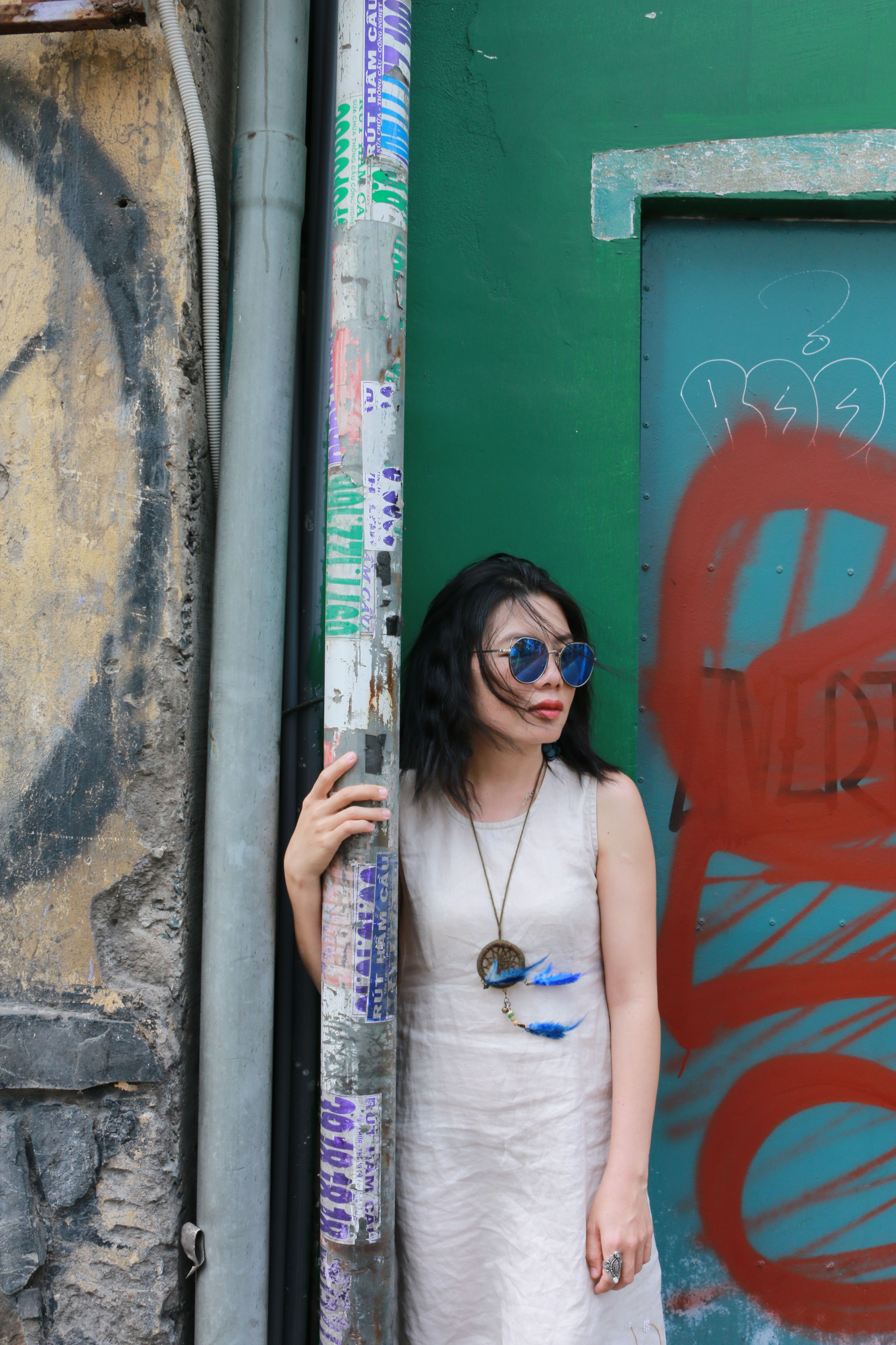 Fashionable woman in sunglasses stands by a graffiti-covered wall in a vibrant Vietnamese city street.