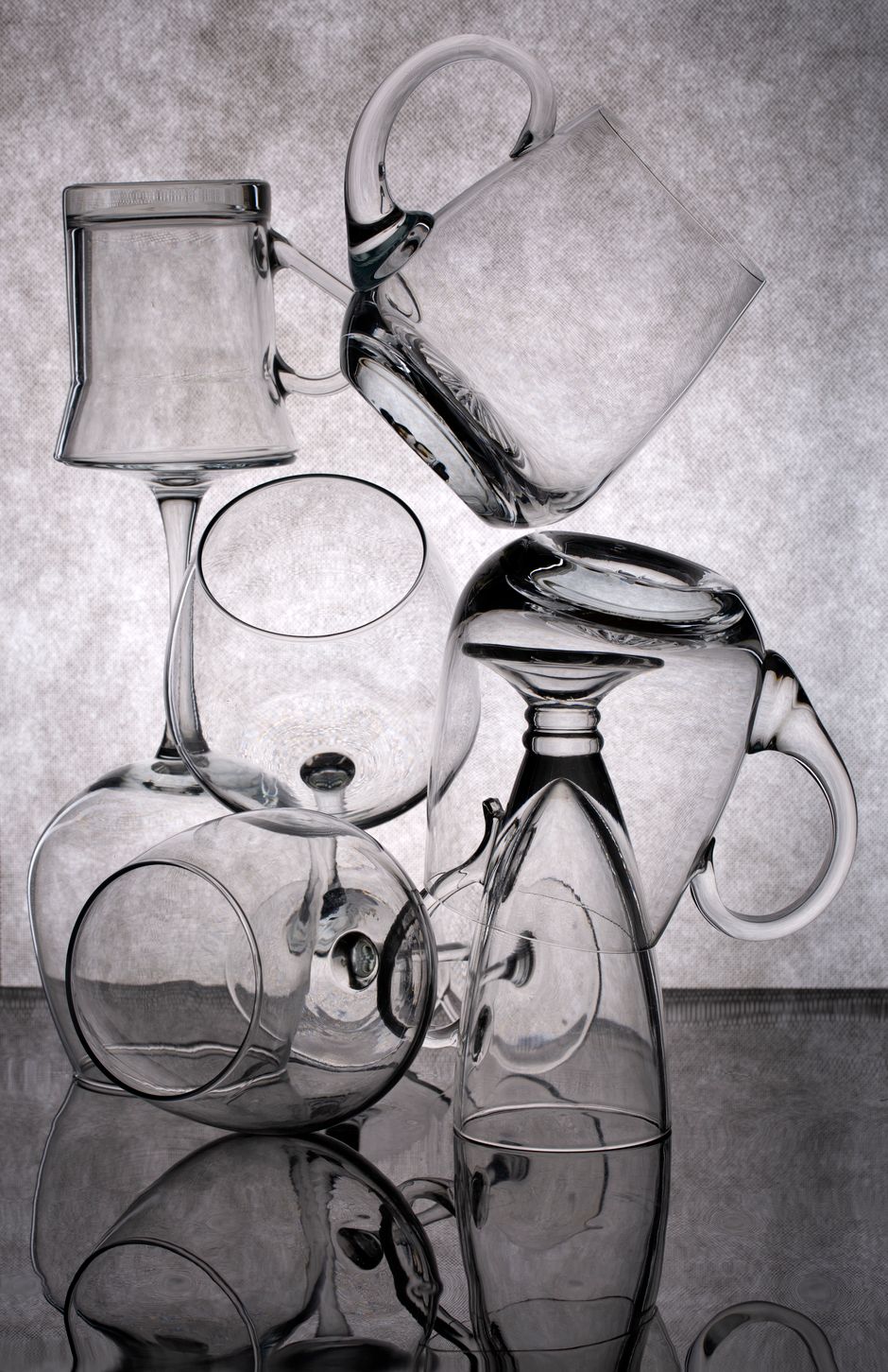 Still life of various glassware creatively stacked on a reflective surface, showcasing elegance in form and transparency.