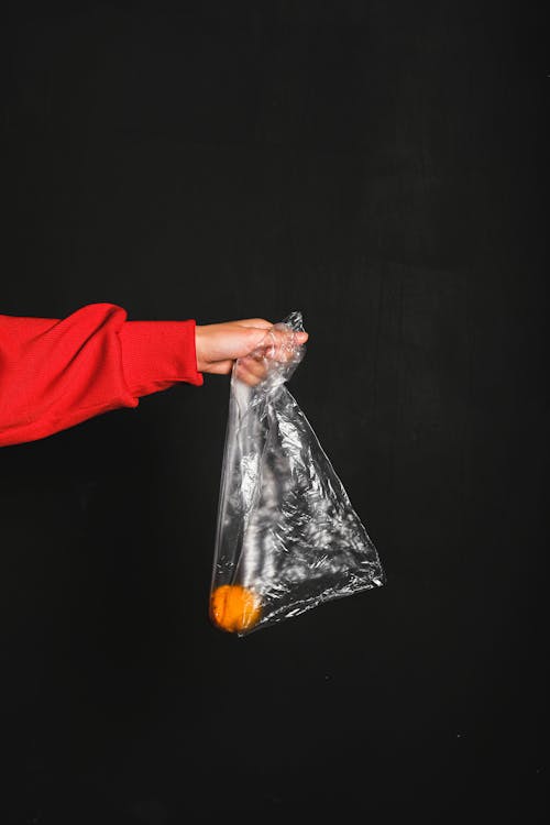 红色长袖上衣的人拿着里面的无色塑料袋和黄色水果