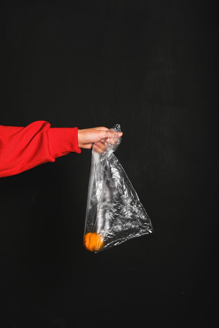 Person In Red Long Sleeve Top Holding Colorless Plastic Bag And Yellow Fruit Inside