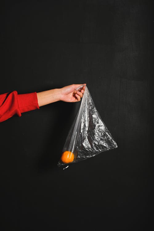 Persona In Camicia A Maniche Lunghe Rossa Che Tiene Il Sacchetto Di Plastica Con Arancia