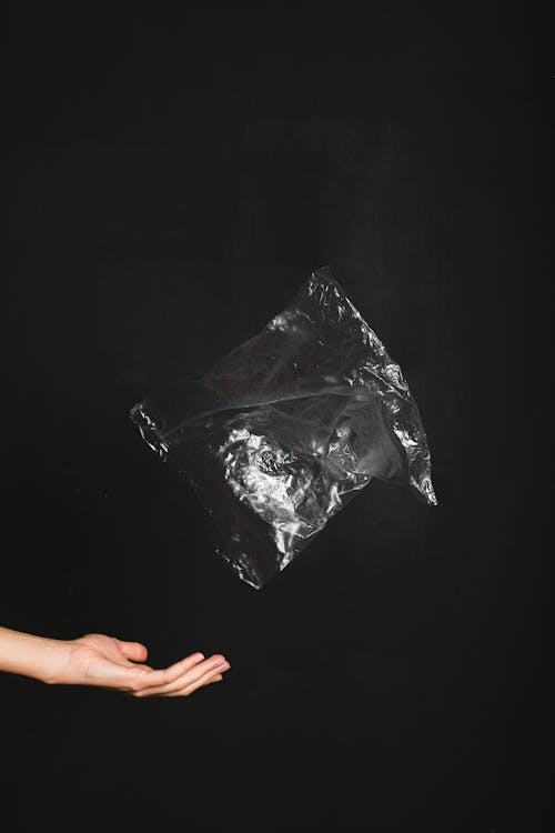 Free A hand tosses a plastic bag against a black background, illustrating environmental concerns. Stock Photo