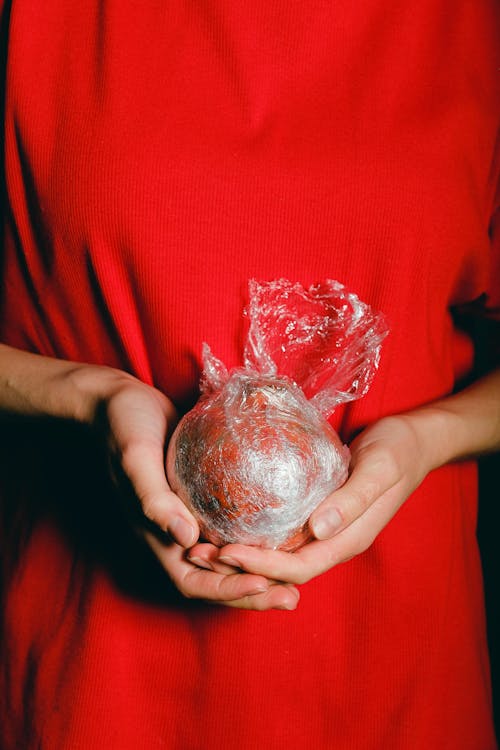 Person in Red Shirt Holding Fruit Covered Plastic