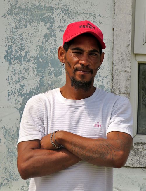 Free Casual portrait of a confident man wearing a red cap and white shirt, standing against a textured wall. Stock Photo