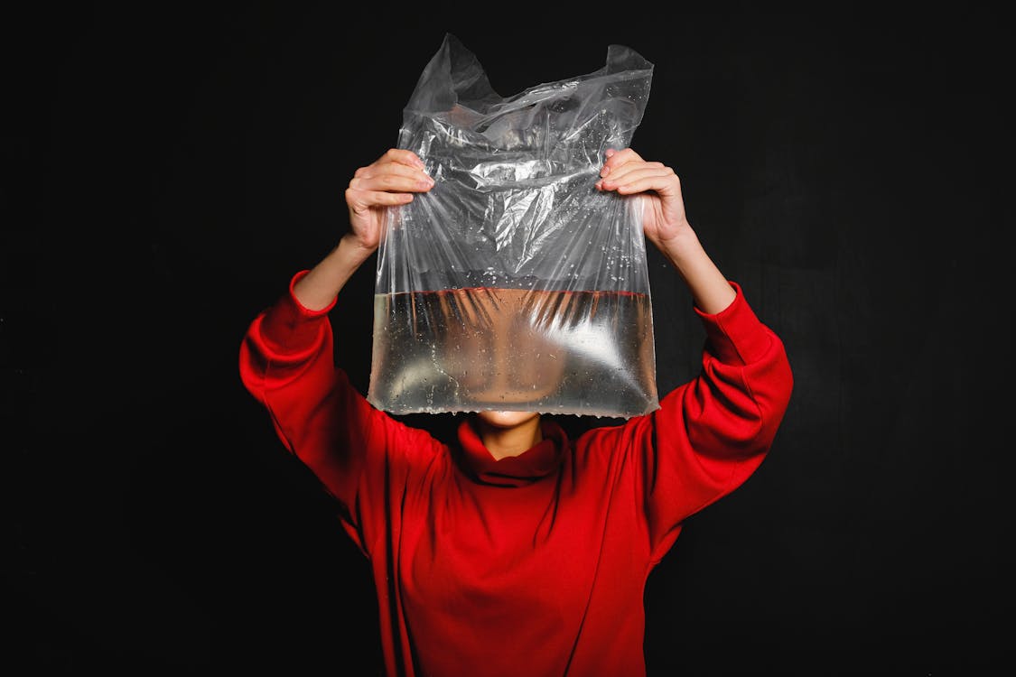 Person in Red Long Sleeve Top Holding Black Plastic Bag with Water Inside