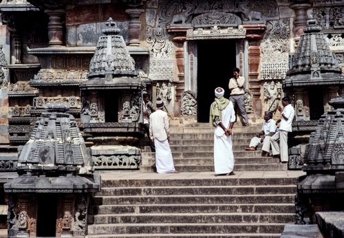 Free Intricate stone sculptures adorn the entrance of an ancient Indian temple, visited by people in traditional attire. Stock Photo
