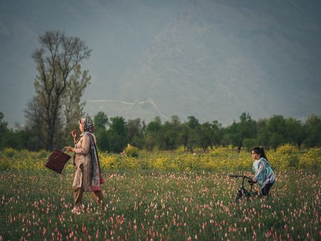 A mother and child walking and biking through a vibrant flower field against a mountainous backdrop.