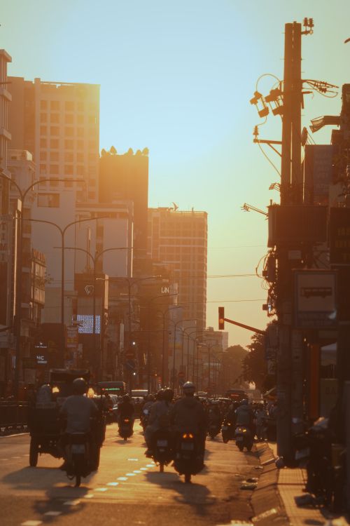 Free Busy urban street scene with motorbikes and city buildings during sunset, capturing dynamic city life. Stock Photo