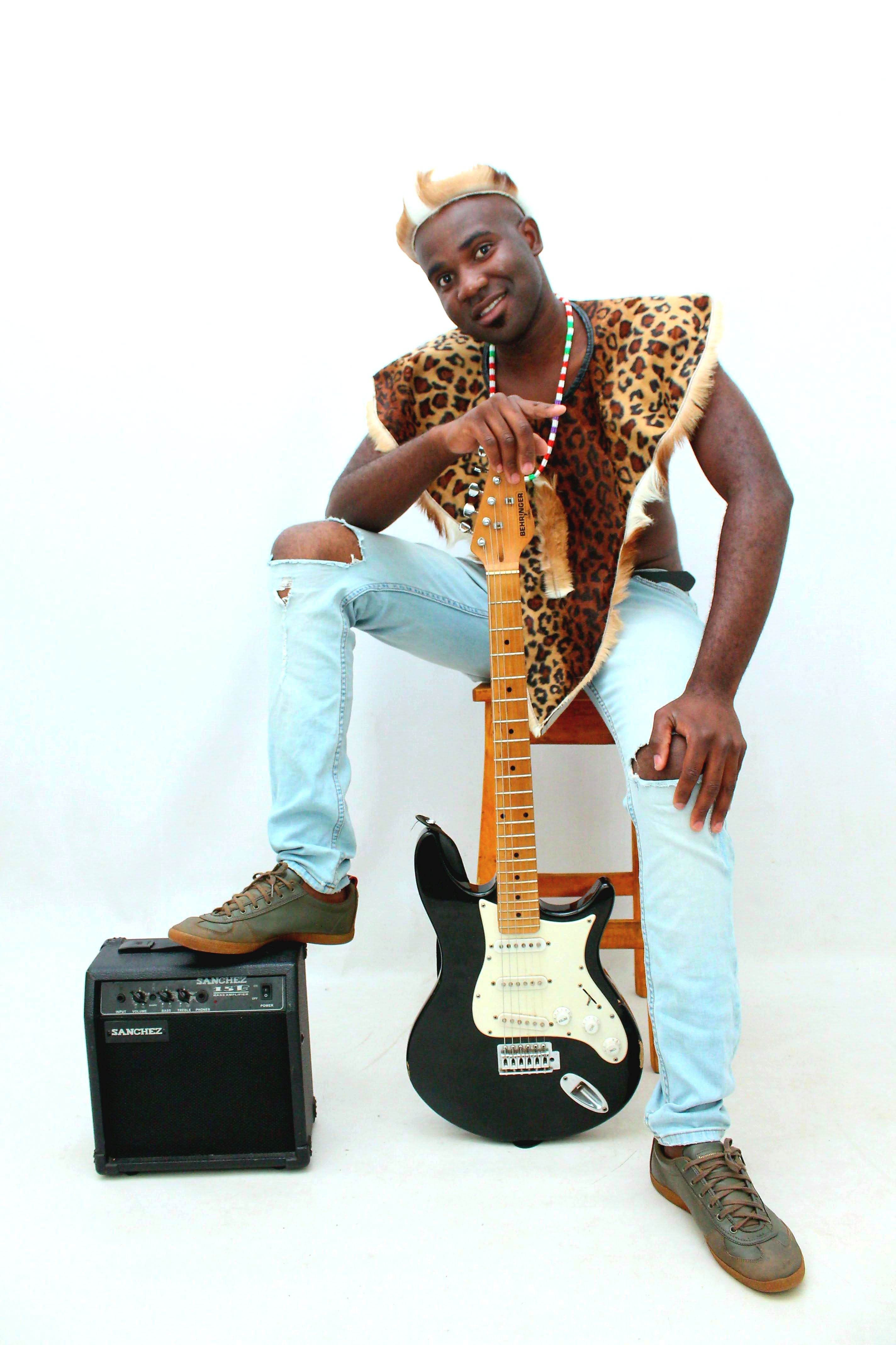 African musician dressed in traditional attire with electric guitar and amplifier on a stool.
