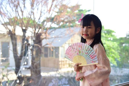 Free Charming portrait of a young girl in traditional pink dress holding a decorative fan indoors. Stock Photo