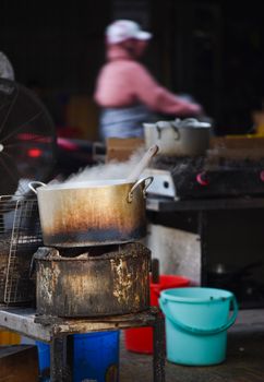 A steaming pot over an open flame in a vibrant Vietnamese street food setting.