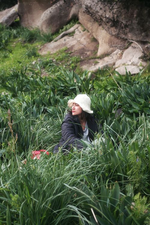 Free A young woman in a hat sits amidst vibrant green foliage in Bodrum, Türkiye. Stock Photo