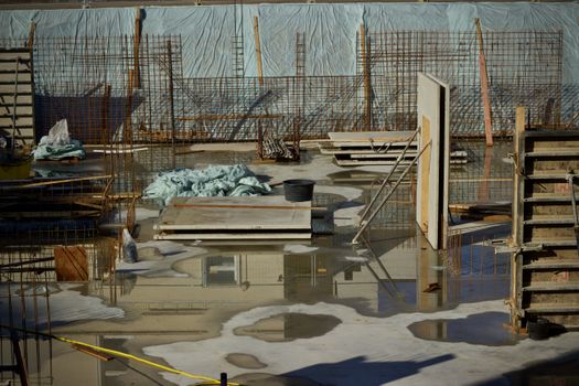 A flooded construction site with scattered materials and visible metal reinforcement.