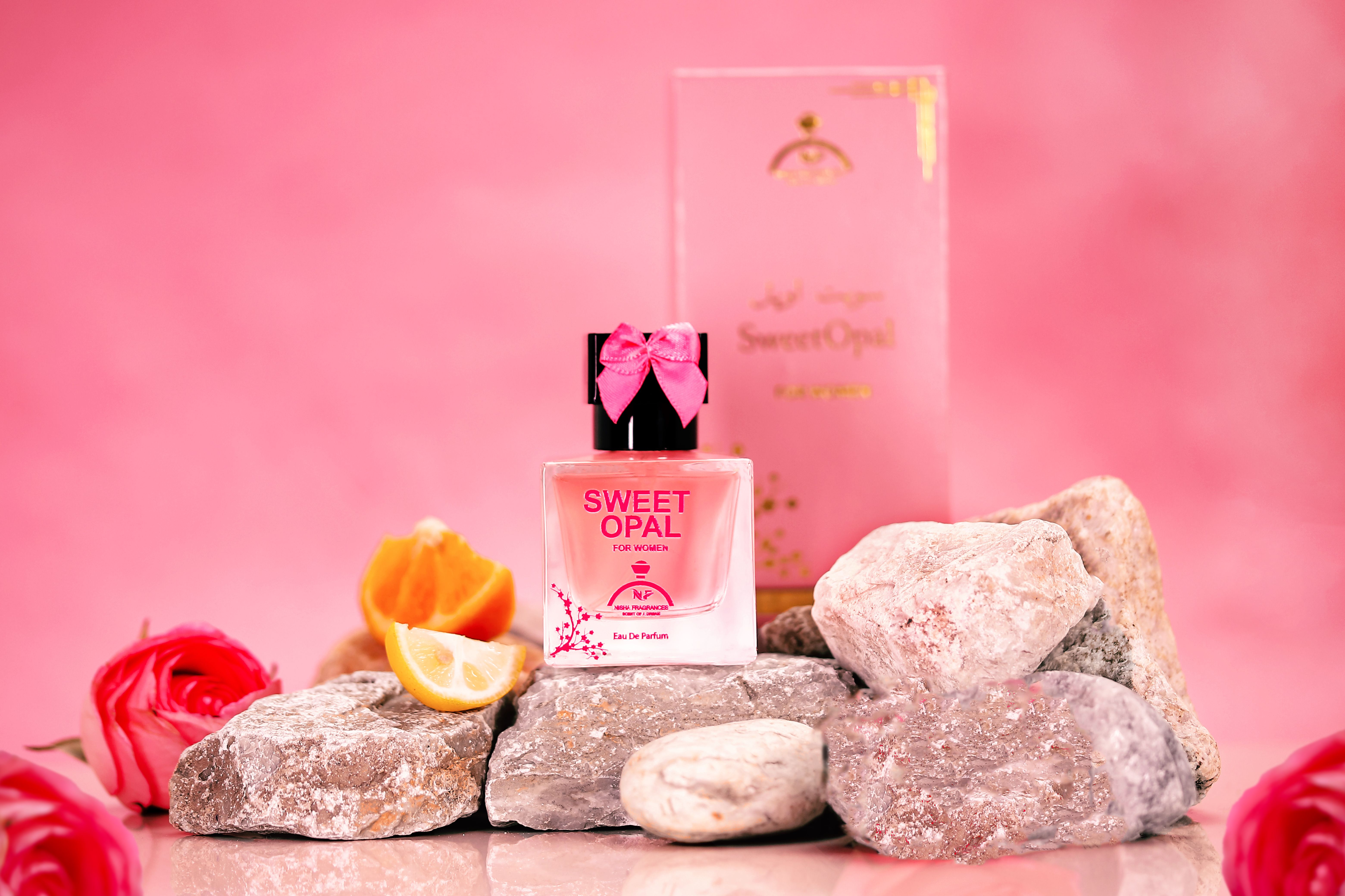 A creative shot of 'Sweet Opal' perfume on rocks with floral decoration and pink background.