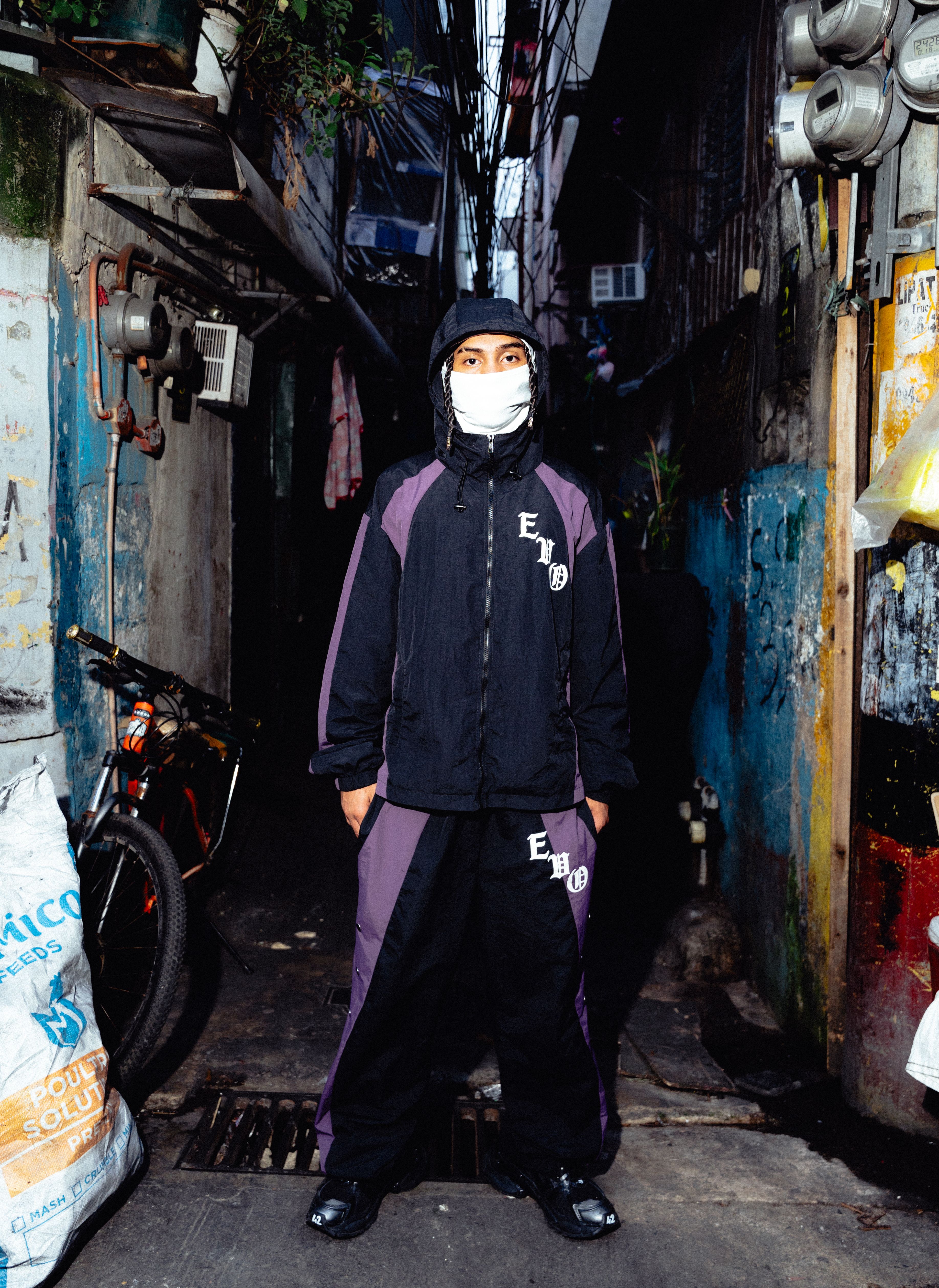 Person in urban streetwear stands confidently in a colorful, narrow alley, exuding modern city vibe.