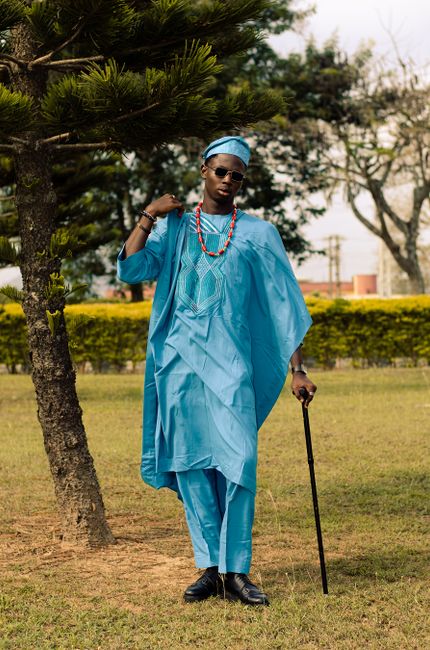 Person in vibrant blue traditional African clothing posing with a cane outdoors.