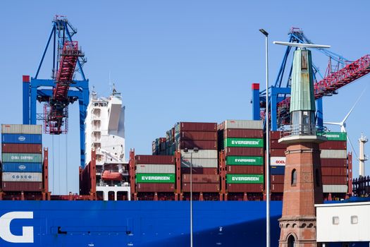 Cargo ship with containers and cranes at Hamburg port on a sunny day.