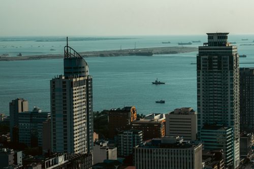 Free Aerial view of a coastal cityscape with modern skyscrapers and cargo ships on the ocean. Stock Photo