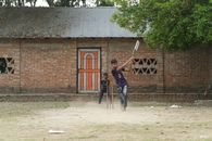 Two boys enjoying a casual game of cricket in a village setting.