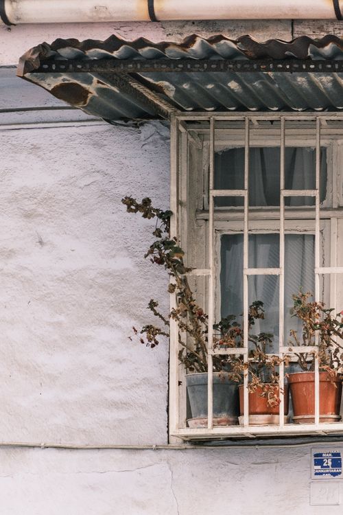 Free A rustic window with metal bars, corrugated metal awning, and potted plants adds charm to a timeless facade. Stock Photo