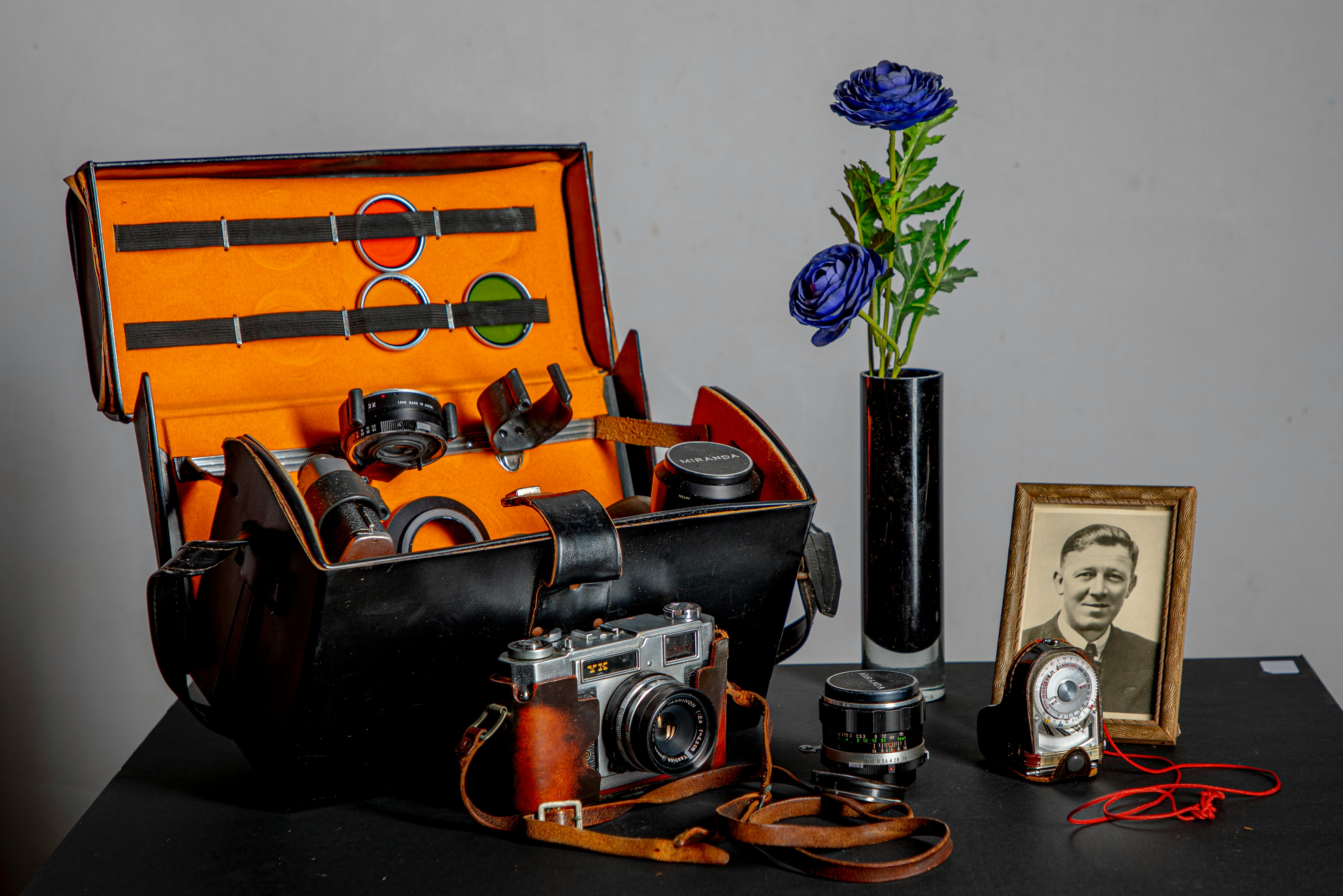 A collection of vintage camera equipment with a portrait and flowers in a vase.