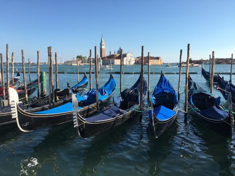 Row of gondolas moored at San Giorgio Maggiore, Venice, under a clear blue sky.