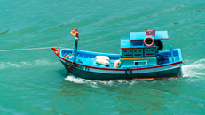 Vibrant fishing boat sailing through turquoise sea waters with flags waving.