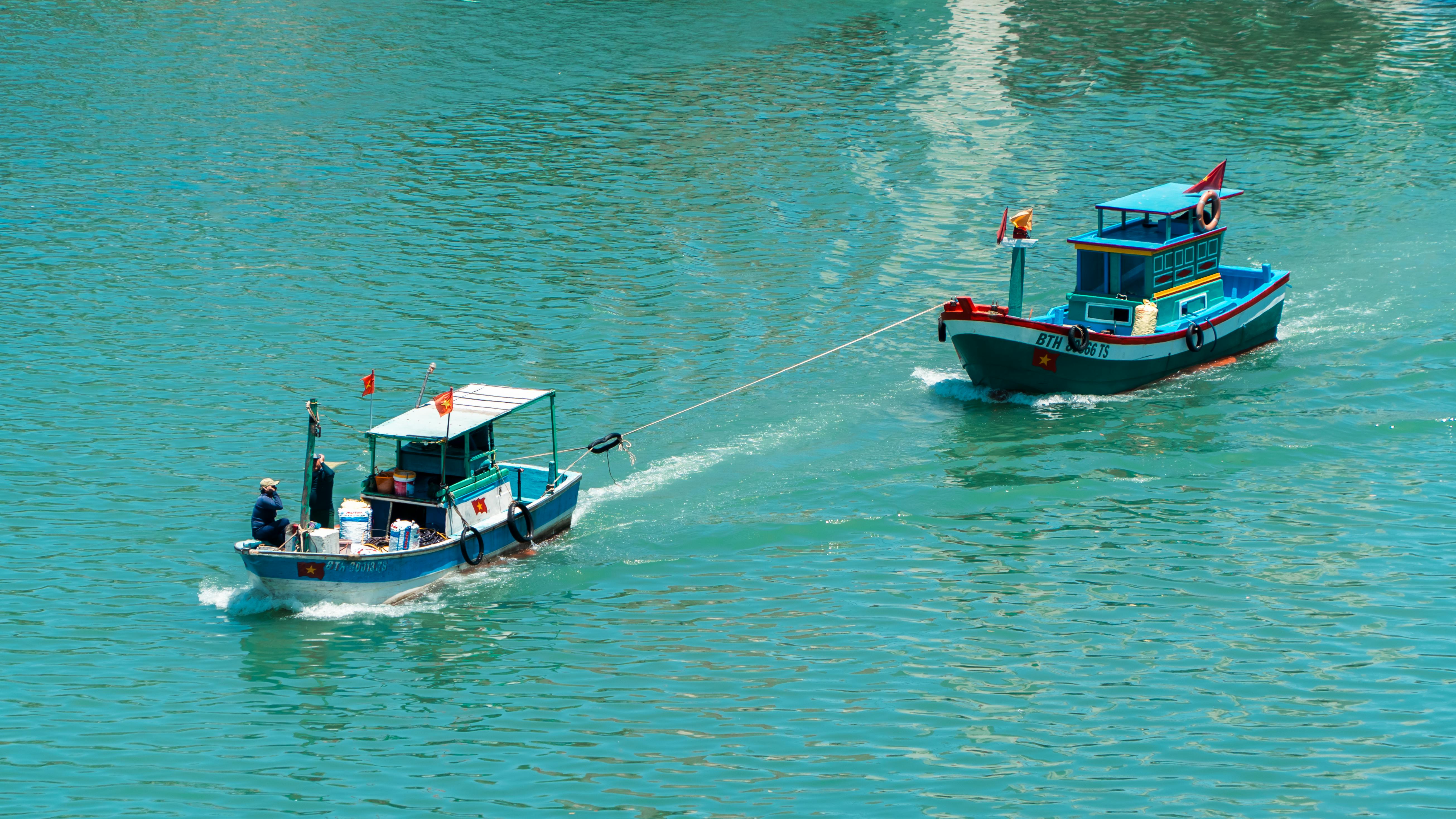 Two fishing boats with flags sailing on clear turquoise waters on a sunny day.