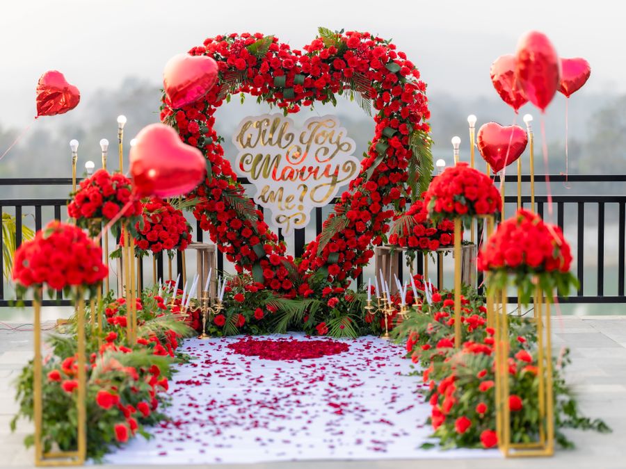 Romantic outdoor proposal setup with heart-shaped roses and red balloons