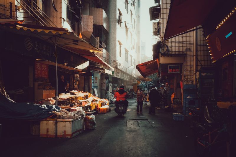 A Guangzhou market street at dusk, stalls lighting up one by one
