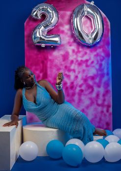 A woman in a blue dress celebrates her 20th birthday with balloons.