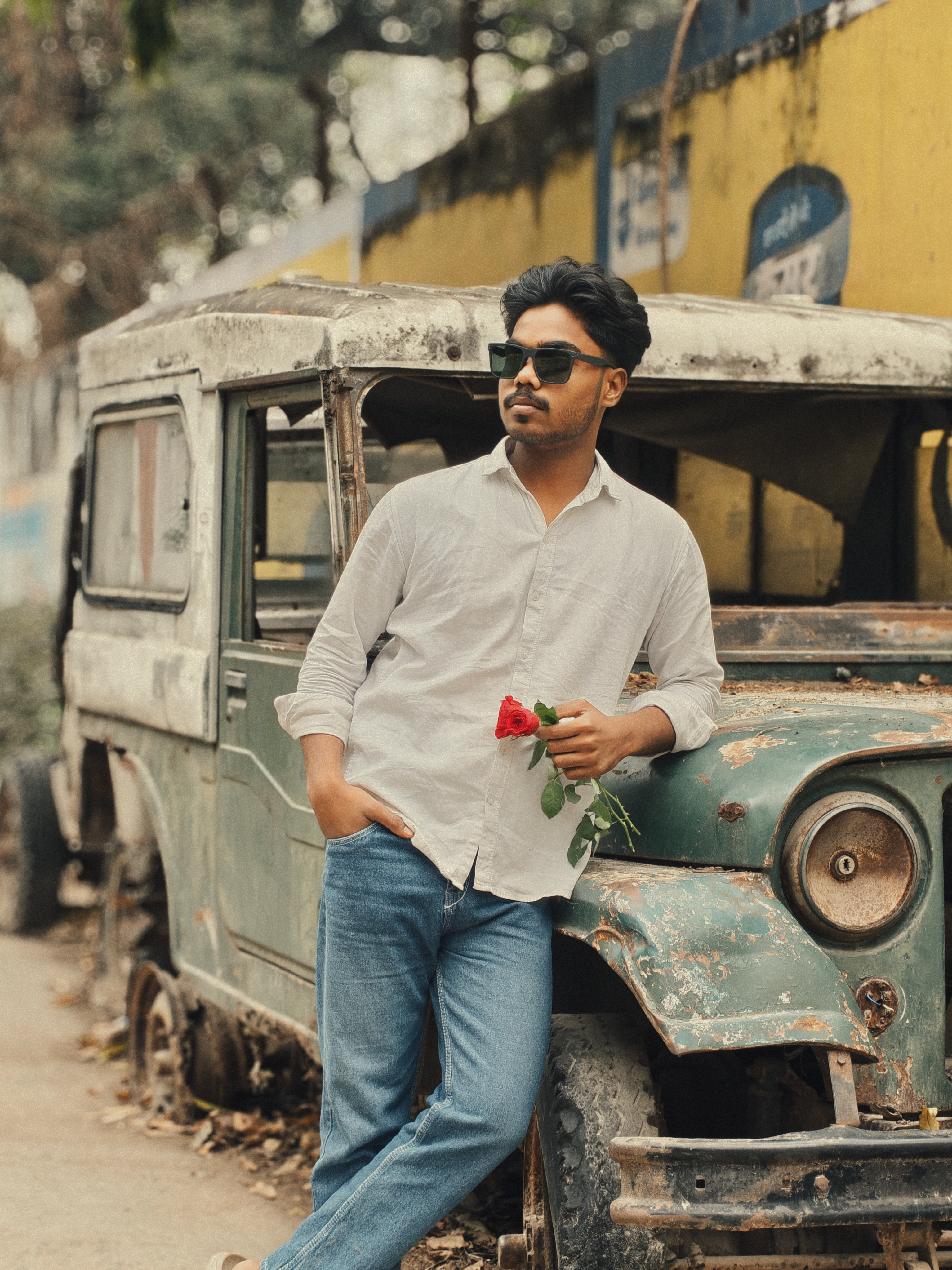 Stylish man with sunglasses leaning on an old car holding a red rose.