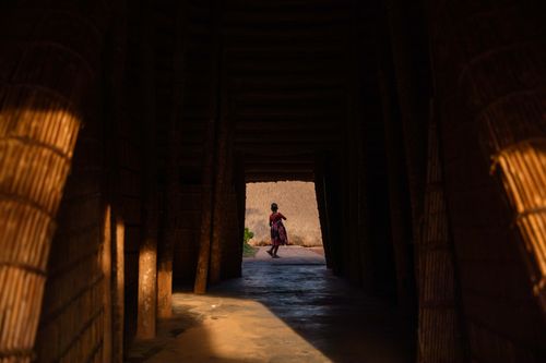 Free A child walks through a traditional wooden structure in Kampala, Uganda, casting long shadows. Stock Photo