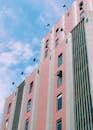 从低角度仰望粉红色摩天大楼，背景是蓝天和云彩