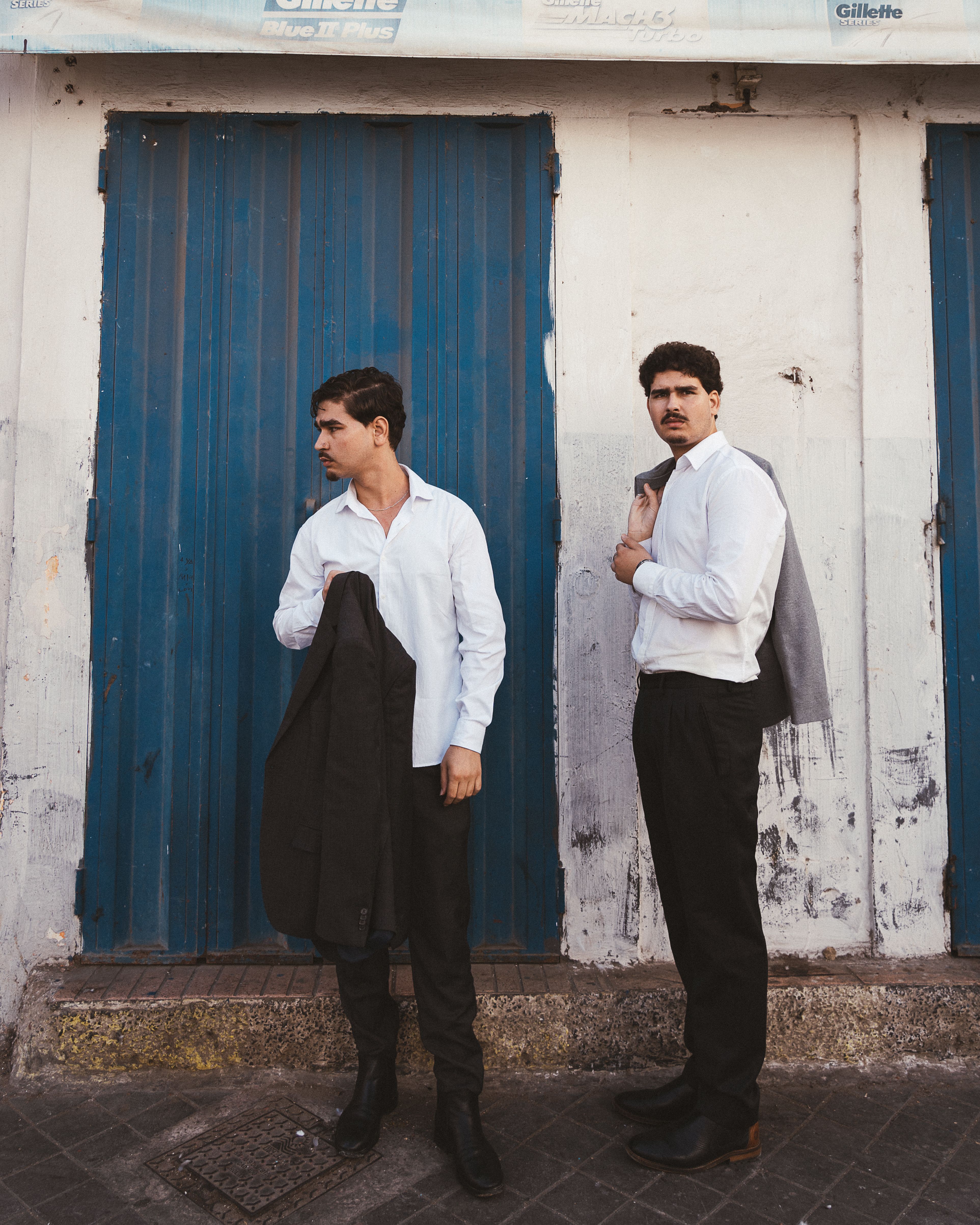 Two men in white shirts and formal pants standing in front of a blue door in Casablanca, Morocco.