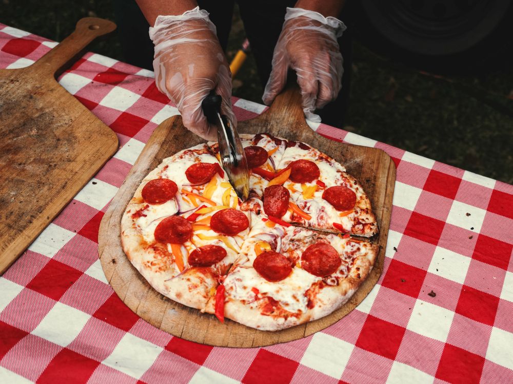 Bucătar tăind o pizza pe o masă cu față de masă în carouri