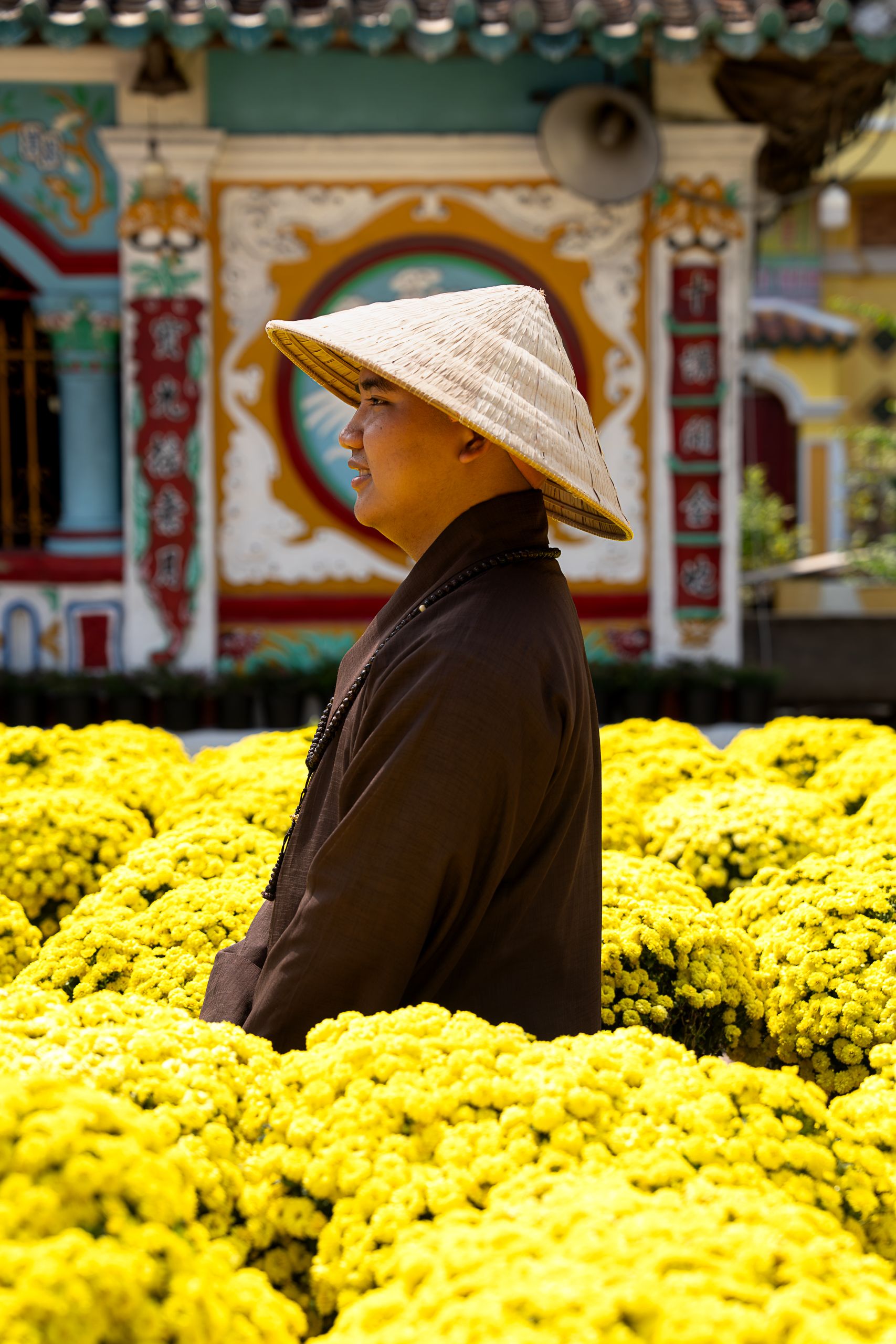 A Vietnamese person in traditional attire stands amidst vibrant yellow chrysanthemums at a cultural site.