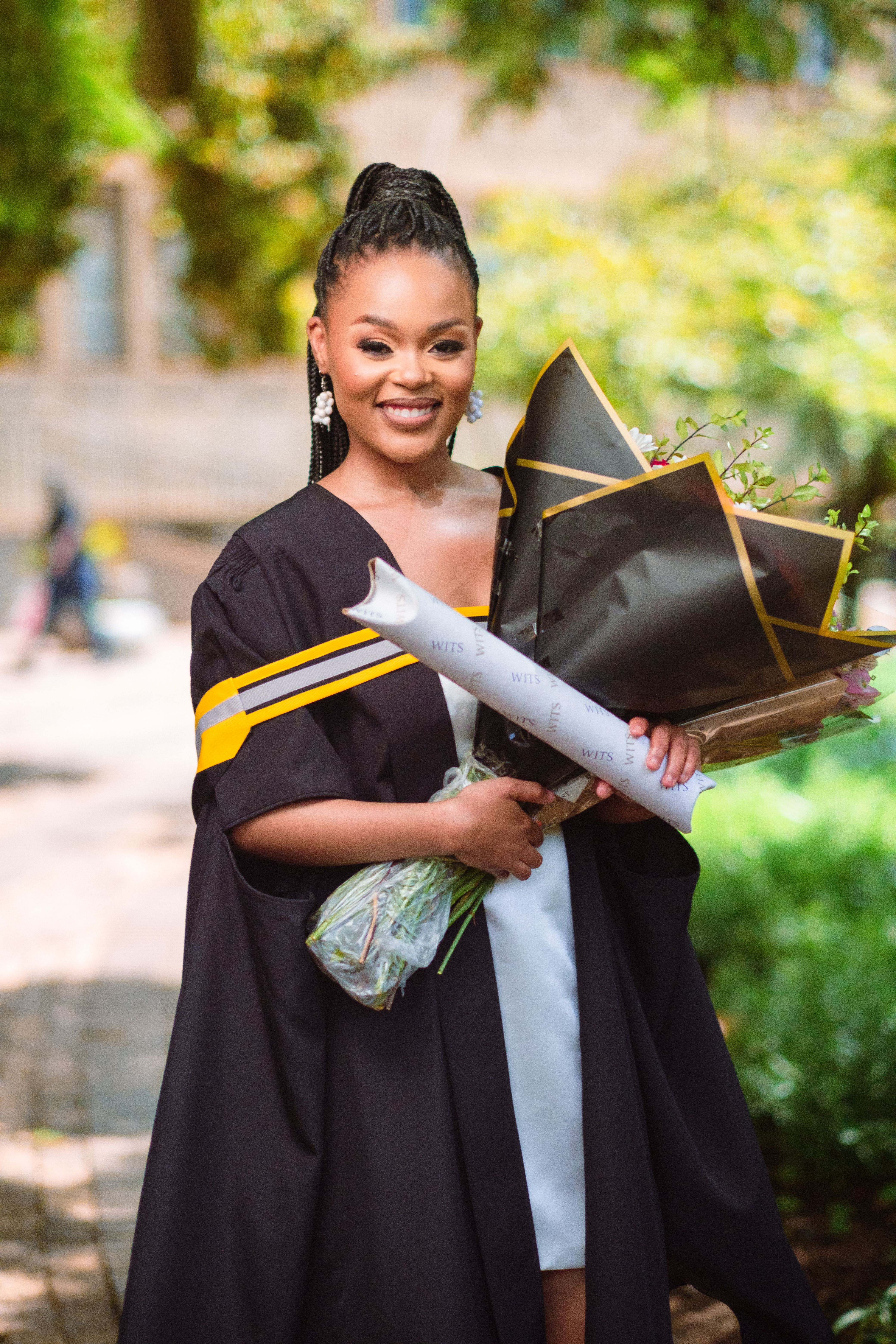 Young graduate celebrating with diploma and flowers outdoors.