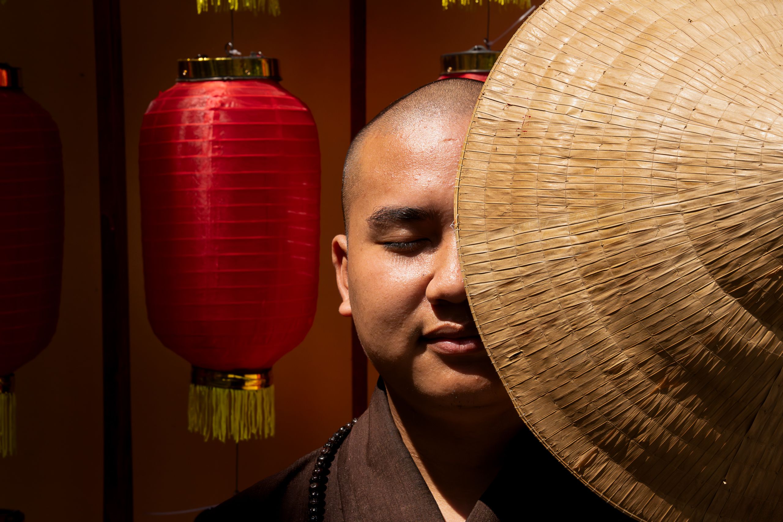 A serene monk in Vietnam with traditional red lanterns and a straw hat creating cultural ambiance.