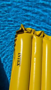 A yellow inflatable mat floating on a sunny afternoon in a blue swimming pool.