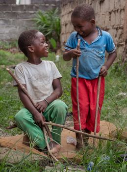 Two smiling children playing with sticks in a grassy outdoor setting.