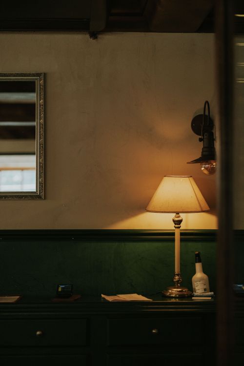 Free A warm, inviting vintage interior featuring a table lamp and framed mirror, perfect for home decor themes. Stock Photo