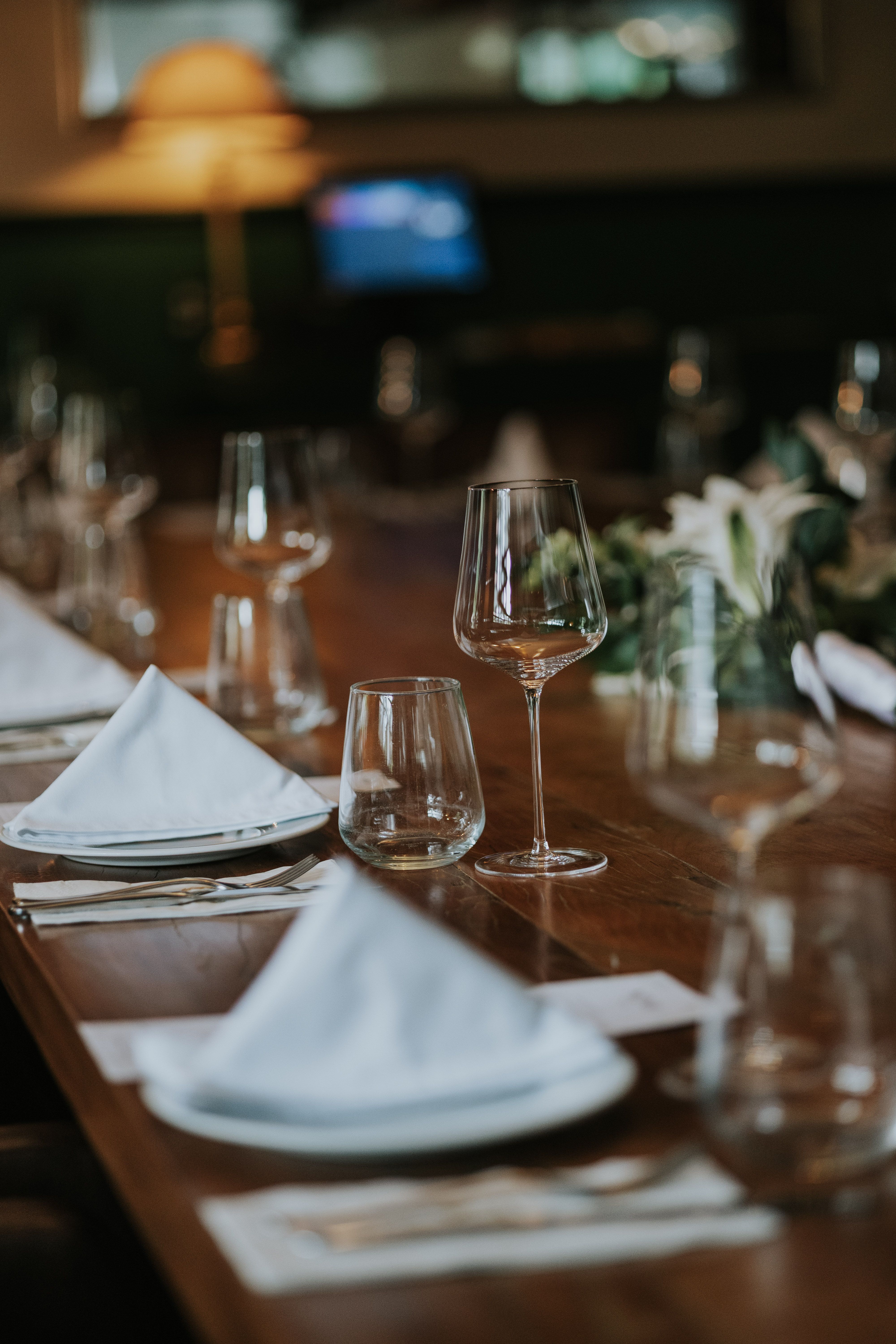 A restaurant table set with wine glasses, white napkins and flowers